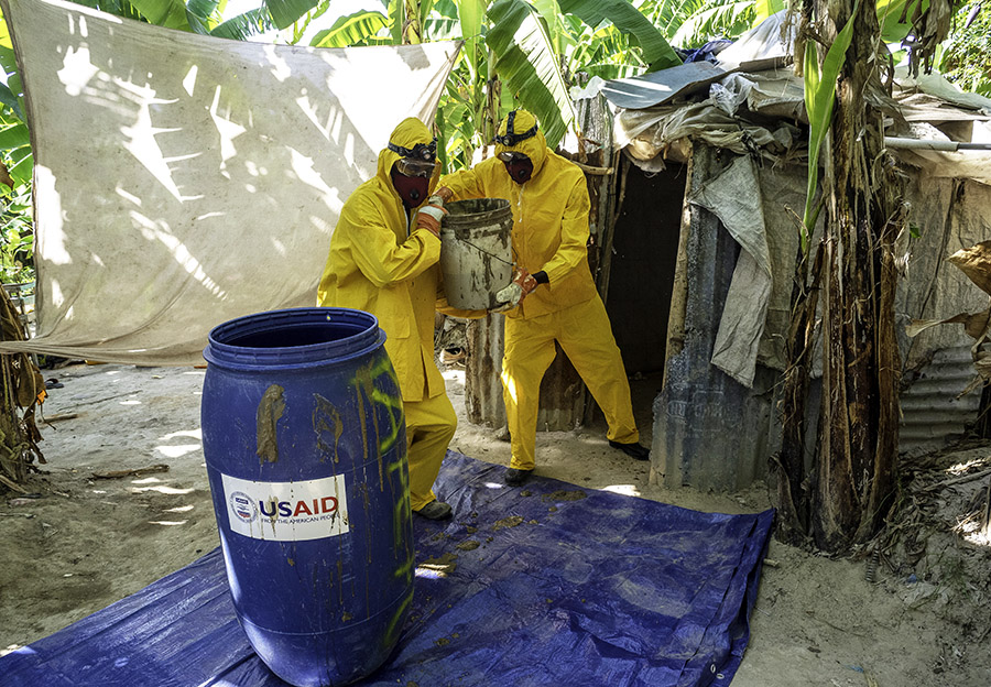 A photo of two workers in protective clothing emptying a latrine